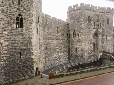 A stone castle with battlements and arched windows with a modern footbridge over a moat at Llety Pen Deitsh 1 in Caernarfon