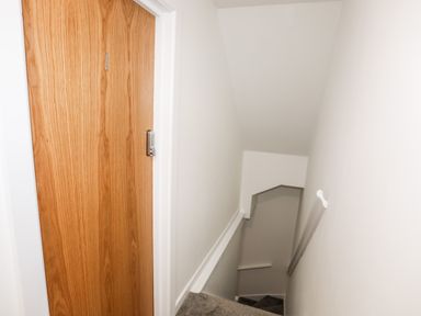 A staircase with a wooden door and white walls at Llety Pen Deitsh 1 in Caernarfon