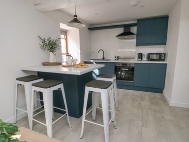A modern kitchen with blue cabinets a white countertop an island with stools and a window at Llety Pen Deitsh 2 in Caernarfon