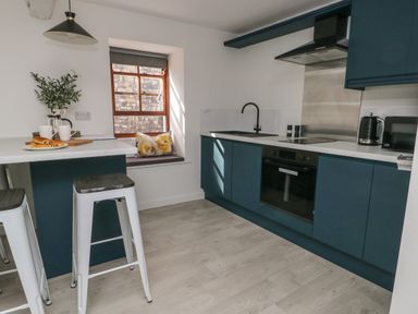 A kitchen with blue cabinets a black sink a window with cushions and two stools at Llety Pen Deitsh 2 in Caernarfon