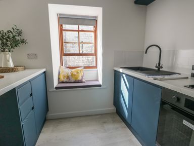 A kitchen with blue cabinets a window seat with cushions and a sink at Llety Pen Deitsh 2 in Caernarfon