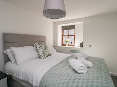 A bedroom with a bed covered in white and green bedding with rolled towels a window with flowers and books at Llety Pen Deitsh 2 in Caernarfon