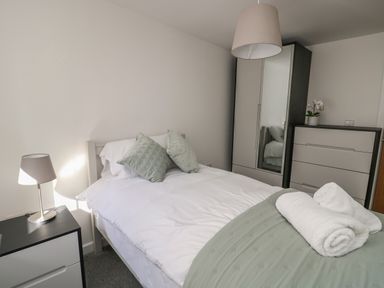 A bedroom with a bed, bedside table with a lamp, wardrobe, and chest of drawers at Llety Pen Deitsh 2 in Caernarfon