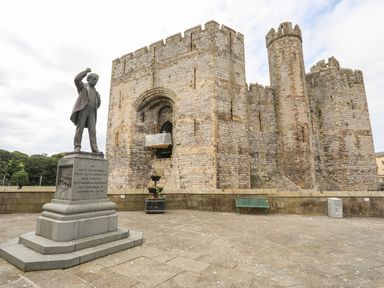 A statue of a man raising his fist outside a stone castle with battlements and arched entrance at Llety Pen Deitsh 2 in Caernarfon