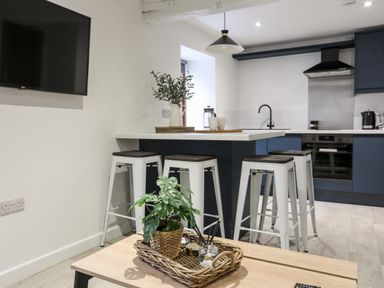 A kitchen with a breakfast bar and stools with a plant on a wooden table at Llety Pen Deitsh 2 in Caernarfon