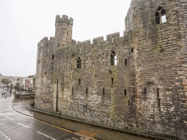An old stone castle wall with towers and narrow windows beside a wet road at Llety Pen Deitsh 2 in Caernarfon