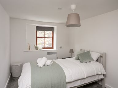 A bedroom with a single bed and two pillows towels on the bed and a window with a blind at Llety Pen Deitsh 2 in Caernarfon