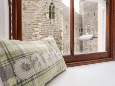 A window seat with a plaid cushion that says cartri and a view of a stone castle wall at Llety Pen Deitsh 2 in Caernarfon