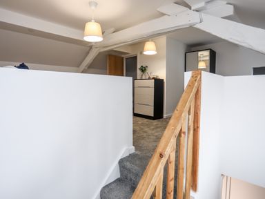 A staircase with wooden railing leading to a hallway with a chest of drawers and ceiling lights at Llety Pen Deitsh 2 in Caernarfon