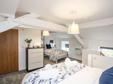 A bedroom with two beds a chest of drawers a wooden door and ceiling beams at Llety Pen Deitsh 2 Caernarfon