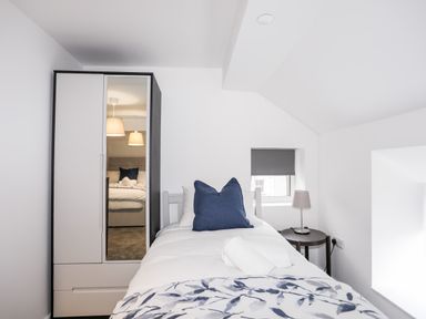 A bedroom with a single bed a wardrobe with mirror and a bedside table with lamp at Llety Pen Deitsh 2 in Caernarfon