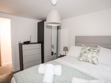 A bedroom with a bed with pillows and rolled towels a chest of drawers a wardrobe with a mirror and a bedside lamp at Llety Pen Deitsh 2 in Caernarfon