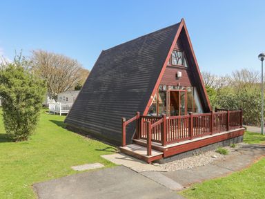 An A-frame cabin with a wooden deck surrounded by grass and trees at 171 Snowdonia View in Chwilog