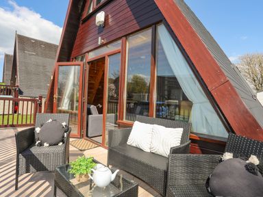 An outdoor patio with black wicker chairs and sofa with cushions a glass table a teapot and plant outside an a frame building at 171 Snowdonia View in Chwilog