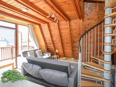 A living area with wooden walls and ceiling featuring a gray sofa set and a spiral staircase at 171 Snowdonia View in Chwilog