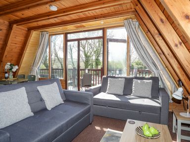 A living room with two grey sofas and a wooden coffee table in front of large windows with curtains at 171 Snowdonia View in Chwilog