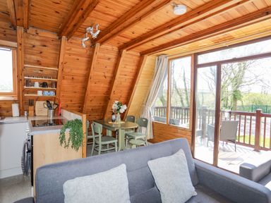 An open kitchen and dining area with wooden walls and ceiling and a gray sofa near a sliding glass door at 171 Snowdonia View in Chwilog