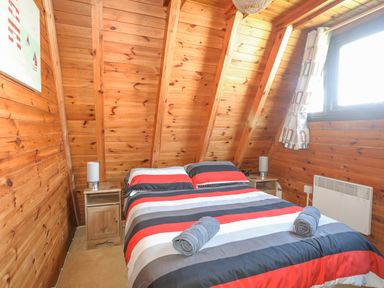 A bedroom with a double bed with striped bedding two rolled towels bedside tables with lamps and wooden walls at 171 Snowdonia View in Chwilog