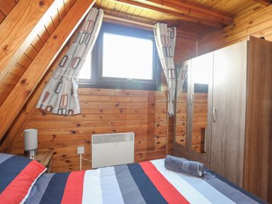 A small bedroom with a striped bedspread a window with curtains and a wardrobe 171 Snowdonia View Chwilog