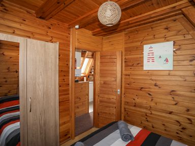 A bedroom with a wooden wardrobe a bed with a striped bedspread and a door leading to another room at 171 Snowdonia View in Chwilog