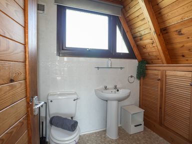 A bathroom with a toilet a sink a window and wooden cabinets at 171 Snowdonia View in Chwilog