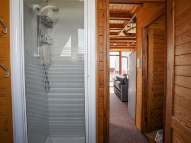 A shower area with glass doors next to a hallway leading to a living room in a wooden cabin at 171 Snowdonia View in Chwilog