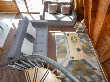 A living room with two grey sofas a coffee table and a spiral staircase at 171 Snowdonia View in Chwilog