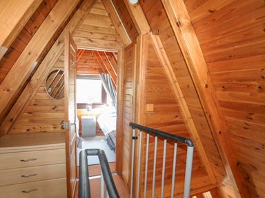 A wooden hallway with a chest of drawers a round mirror stairs with a safety gate and a bedroom visible through an open door at 171 Snowdonia View in Chwilog