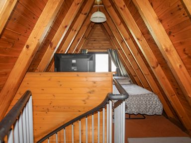 A narrow attic bedroom with wooden walls and ceiling a single bed with patterned bedding a television on a wooden partition and metal railing at 171 Snowdonia View in Chwilog