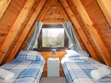 A bedroom with two single beds with blue plaid bedding and a window with curtains at 171 Snowdonia View in Chwilog