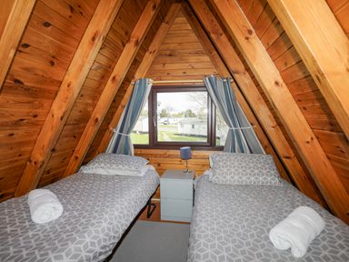 A wooden bedroom with two single beds and a window with blue striped curtains at 171 Snowdonia View in Chwilog