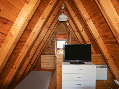 A wooden attic room with a white chest of drawers with a television on top and a light fixture hanging from the ceiling at 171 Snowdonia View in Chwilog