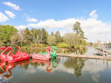 A dock with red and green swan pedal boats on a lake with trees and a wooden pier at 171 Snowdonia View in Chwilog