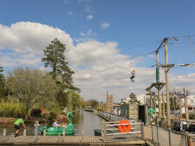 An outdoor adventure park with people on a green dragon boat in a water canal and a person on a zip line above the water at 171 Snowdonia View in Chwilog