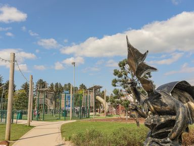 An outdoor playground with climbing structures and a dragon statue near a paved pathway