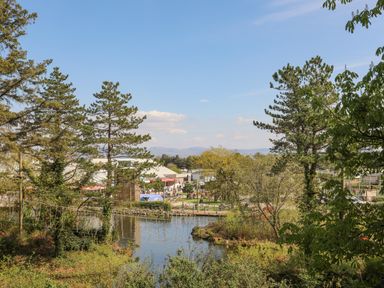 A park with a pond a rope bridge and trees in the foreground and buildings and people in the background at 171 Snowdonia View in Chwilog