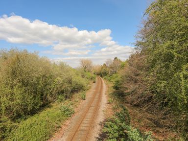 Railway tracks running through dense trees and bushes under a partly cloudy sky at 171 Snowdonia View in Chwilog