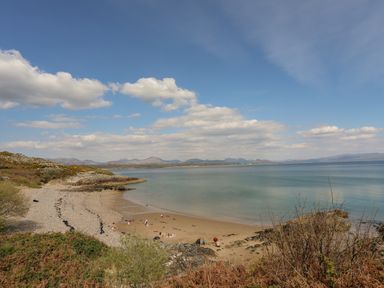 A beach with people on sand and pebbles near calm water and hills in the distance at 171 Snowdonia View in Chwilog
