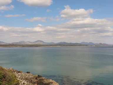 A coastal view with rocky shoreline and distant hills under a cloudy sky at 171 Snowdonia View in Chwilog