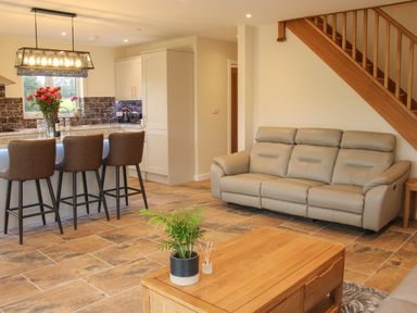 An open plan living area with a leather sofa a wooden coffee table and bar stools at Holly Lodge in Forden near Montgomery