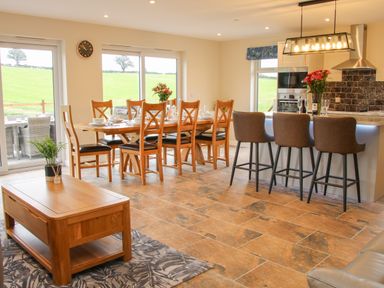 A dining area with wooden table and chairs next to a kitchen island with three bar stools at Holly Lodge in Forden near Montgomery