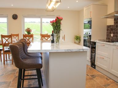 A kitchen with a marble countertop island and brown chairs near a dining table by large windows at Holly Lodge in Forden near Montgomery