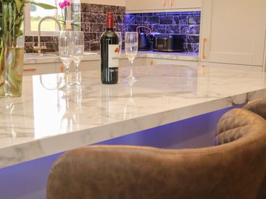 A kitchen countertop with a wine bottle and glasses near a sink and black tiled wall at Holly Lodge in Forden near Montgomery