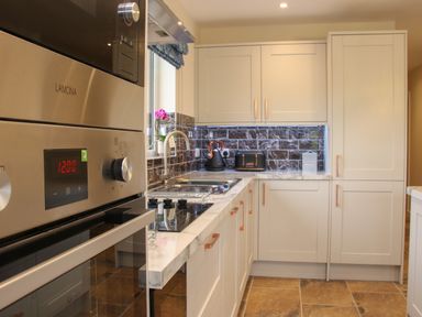 A kitchen with white cabinets a stainless steel oven a sink toaster and kettle on the countertop at Holly Lodge in Forden near Montgomery