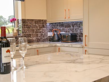 A kitchen with marble countertops, cream cabinets with orange handles, a black kettle, a black toaster, and a bottle of wine with two wine glasses at Holly Lodge in Forden near Montgomery