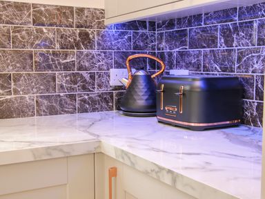 A kitchen countertop with a black kettle and black toaster against a dark marbled tile backsplash at Holly Lodge in Forden near Montgomery