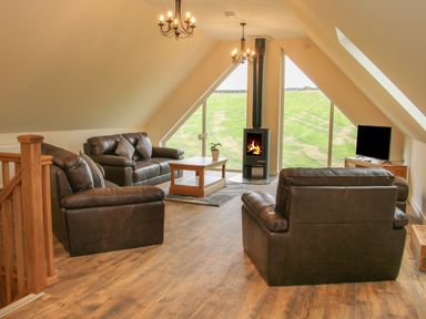 A living room with leather sofas a wooden coffee table a wood stove and a television at Holly Lodge in Forden near Montgomery