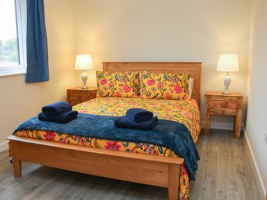 A bedroom with a wooden bed with floral bedding two bedside tables with lamps and folded towels on the bed at Holly Lodge in Forden near Montgomery