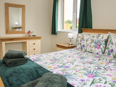 A bedroom with a floral bedspread green curtains a wooden dressing table with a mirror and folded towels on the bed at Holly Lodge in Forden near Montgomery