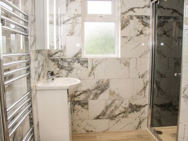 A bathroom with a sink cabinet a chrome heated towel rail a glass shower enclosure and tiled walls at Holly Lodge in Forden near Montgomery